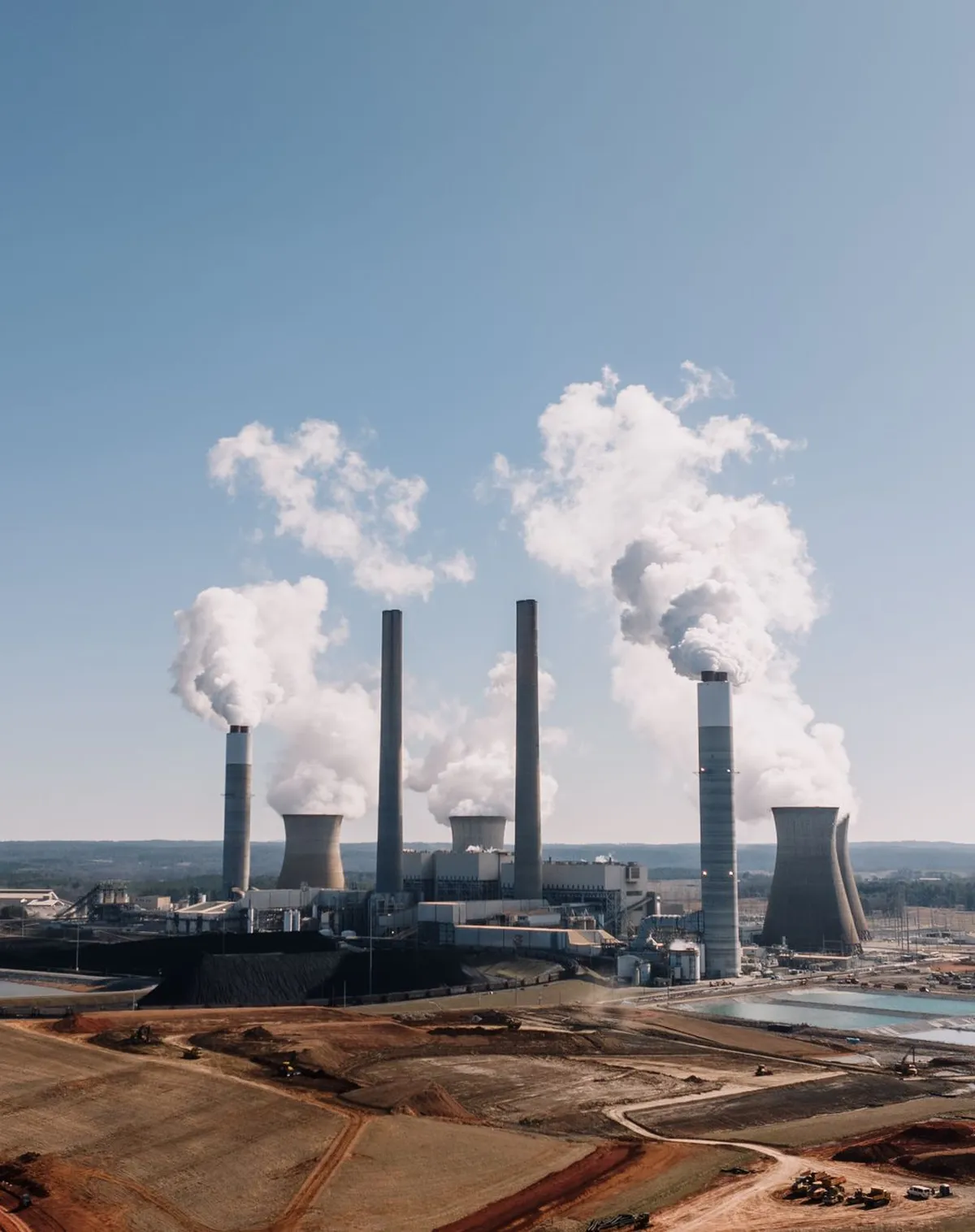 Planta industrial vista de distância, com chaminés e fumaça clara em operação — fotografia ilustrativa Pexels